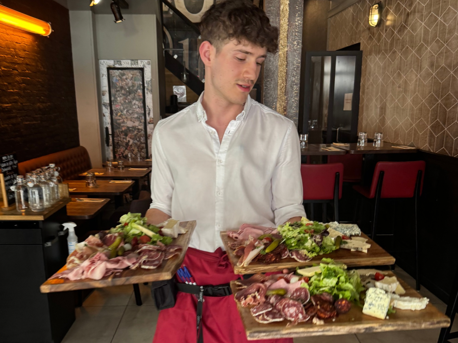 Serveur souriant regardant trois assiettes gourmandes, accueil chaleureux au restaurant L'Annexe Chartres