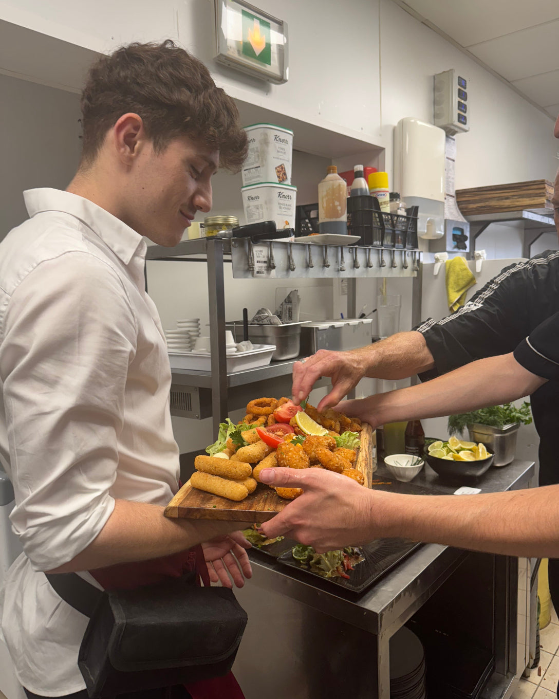 Serveur de L’Annexe recevant une grande planche apéritif chaud avec frites, onion rings et assortiments, préparée en cuisine