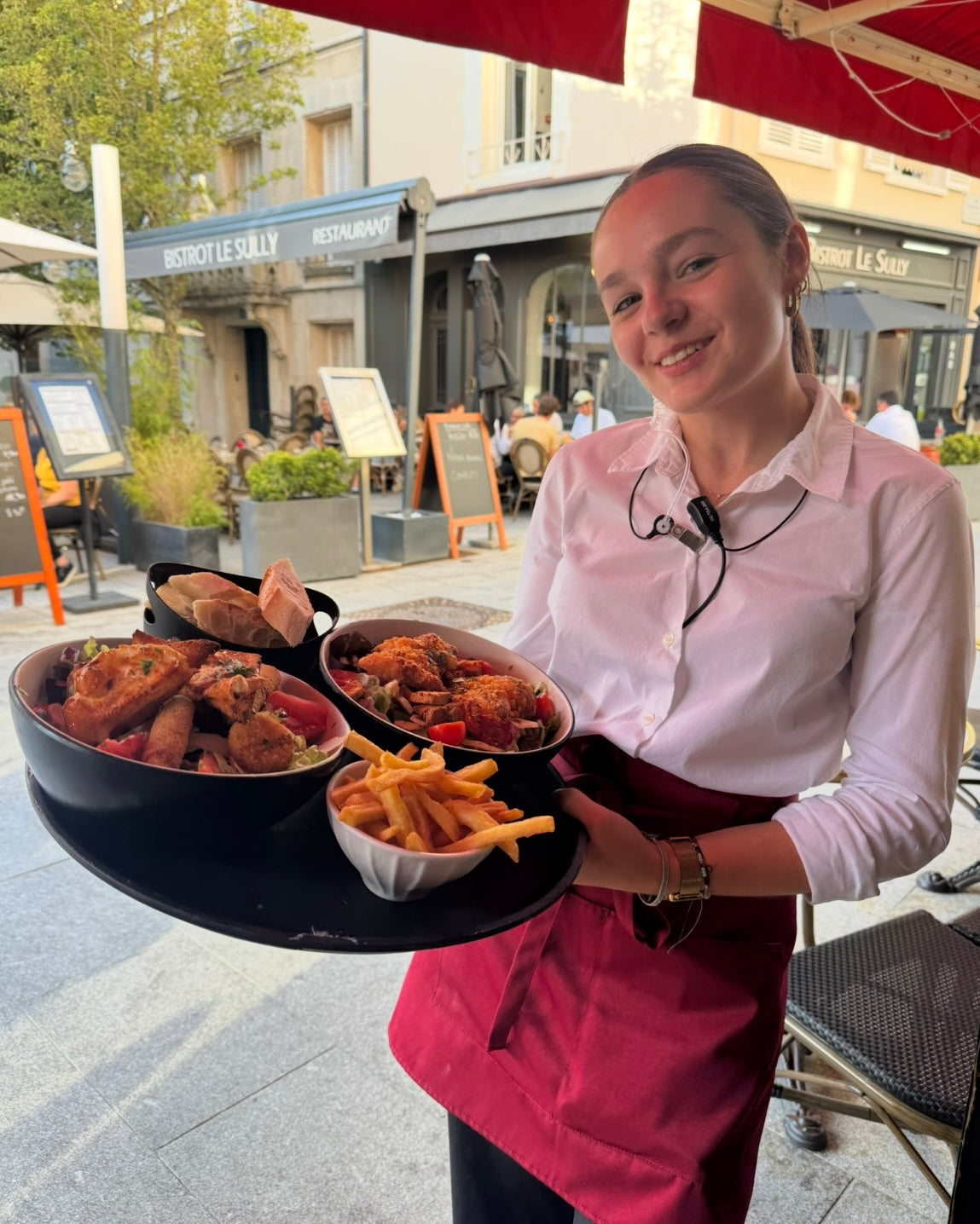 Serveuse souriante avec des plats variés et frites maison sur la terrasse de L'Annexe Chartres