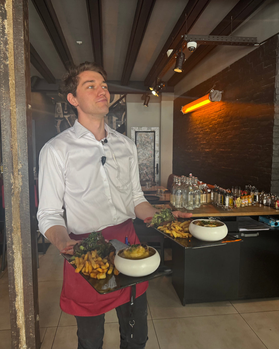 Serveur de L’Annexe portant des assiettes de frites et plats maison dans la salle du restaurant à Chartres, juillet 2025.